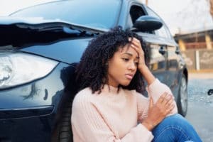 woman sits against her damaged car after a wreck