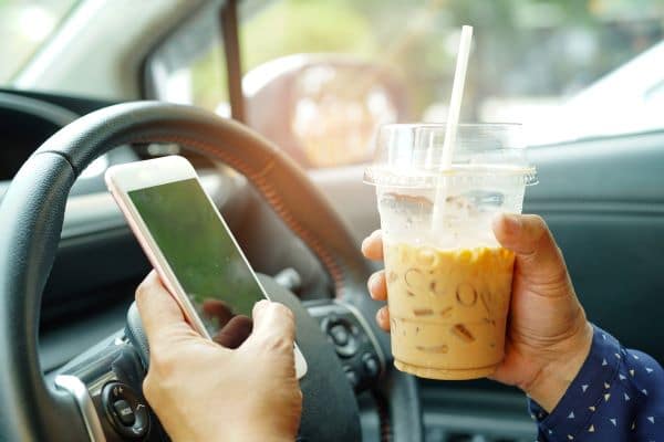 A distracted driver texts with one hand and holds an iced coffee in the other hand