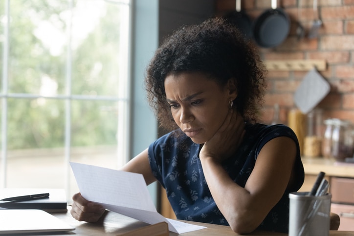 A woman seated at a table indoors rests her head on her palm and gazes seriously at a document