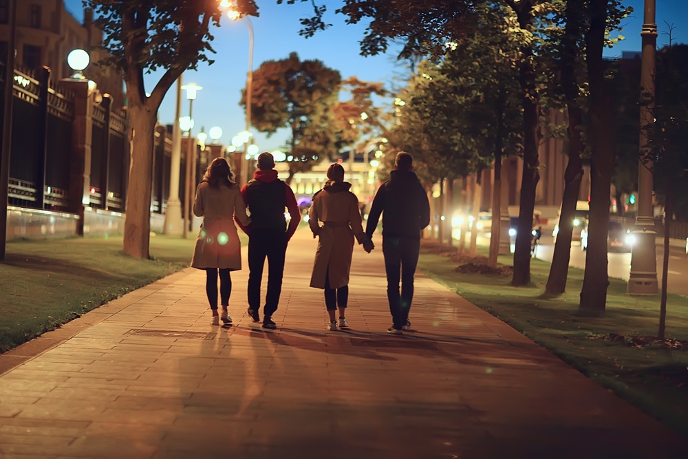 Two couples in fall coats walk down a pedestrian walkway at dusk