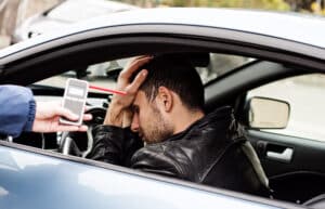 Man behind the wheel of car as officer holds out breathalyzer test for DWI